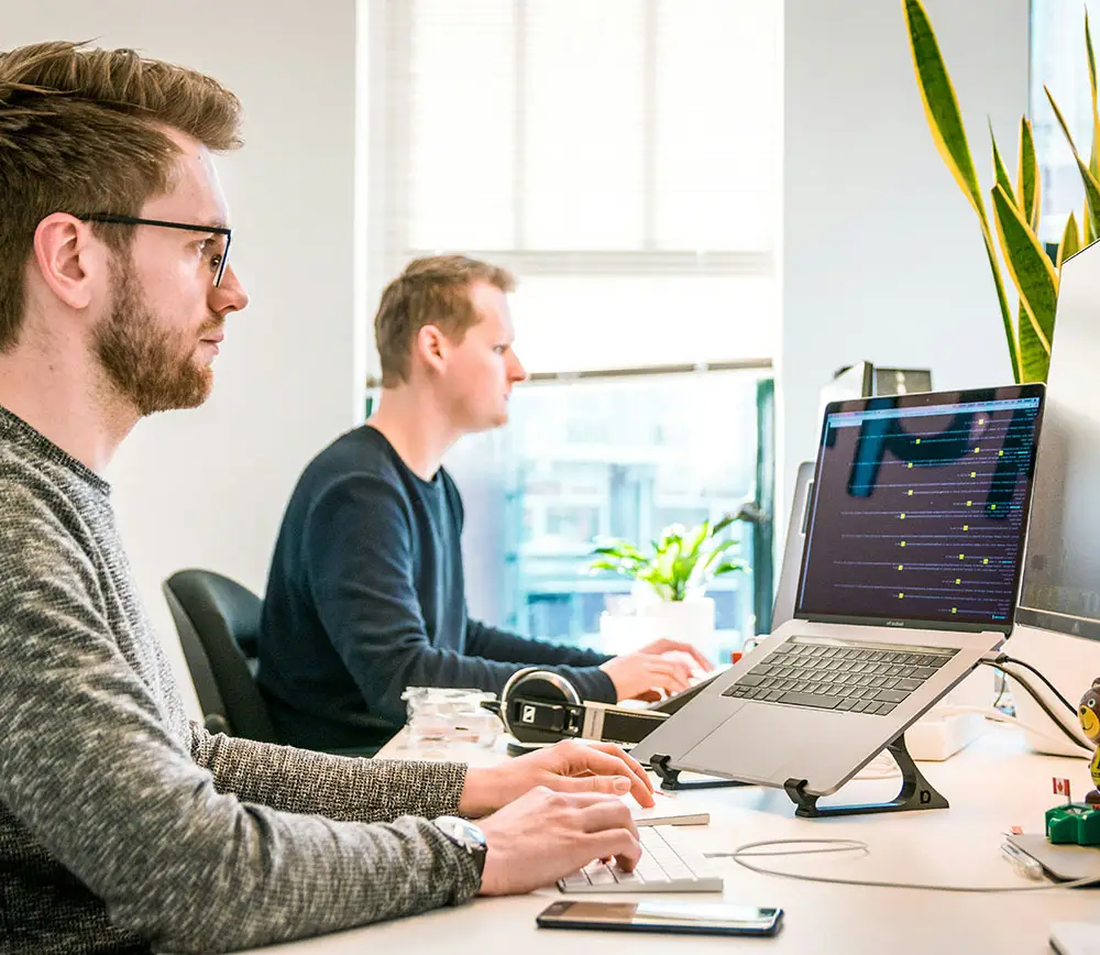 Two men working on laptops in a bright office